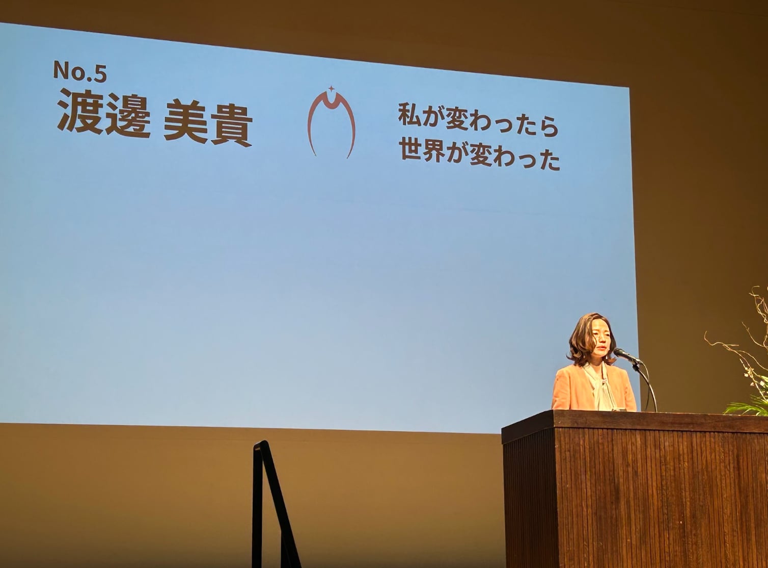 大きなスクリーンの前で講演する渡邊美貴さん